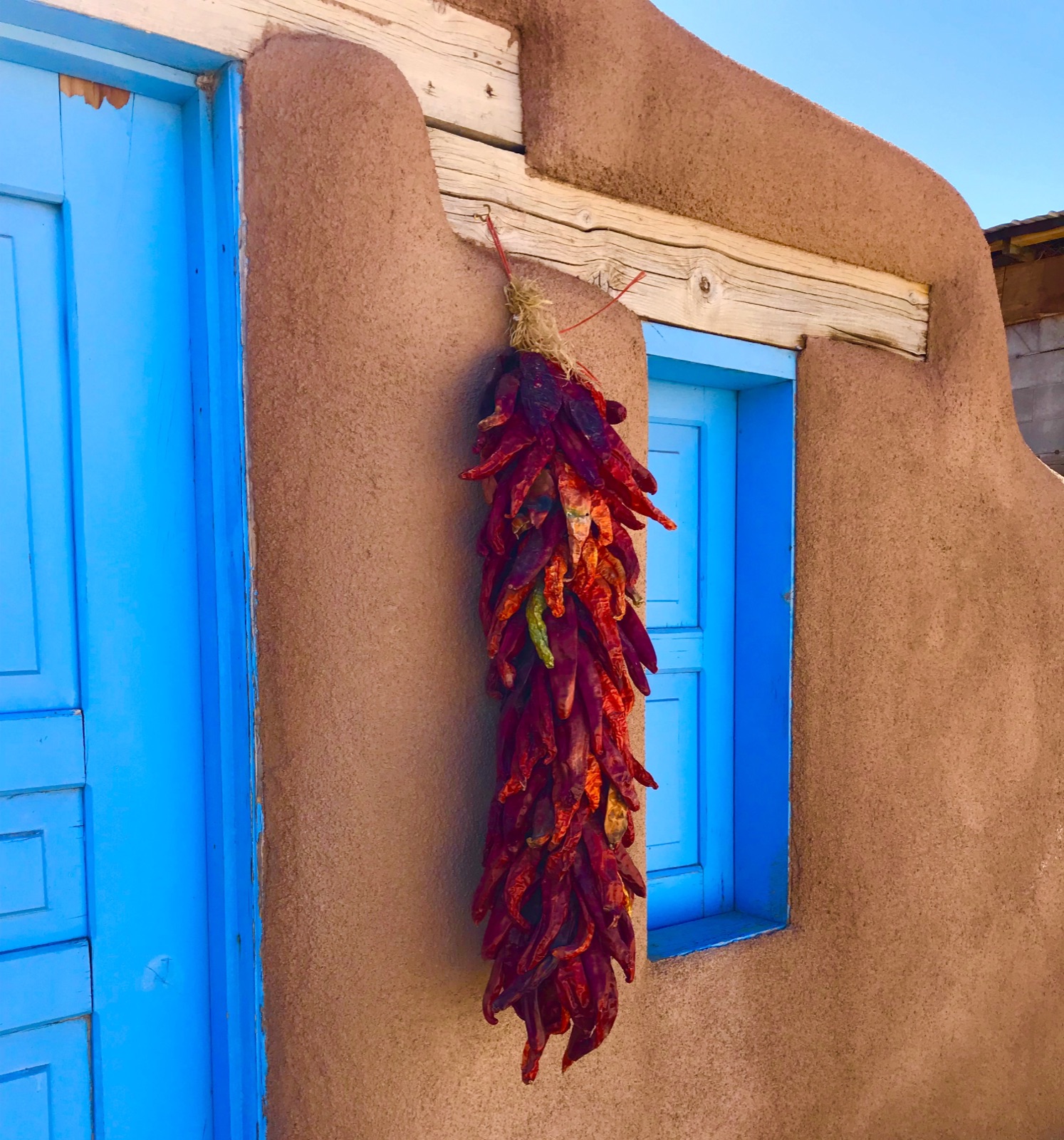 Adobe wall with bright blue window frame and red chile ristra